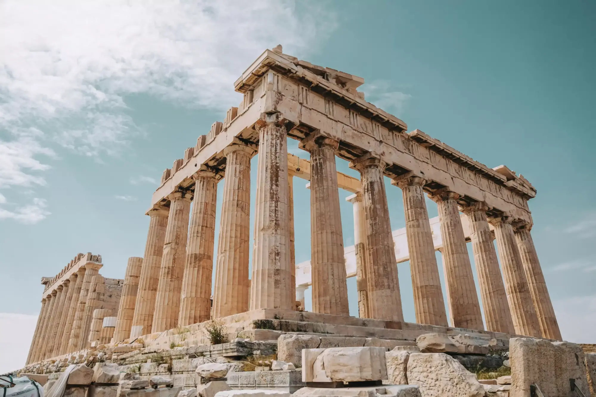Atina'daki Parthenon Tapınağı'nın alt açılı çekiminde, gökyüzüne doğru yükselen devasa, yivli sütunları ve yıpranmış taş işçiliği, Antik Yunan mimarisinin ihtişamını ve zamanın izlerini taşıyan ayrıntılarıyla belirgin bir şekilde görülmektedir.