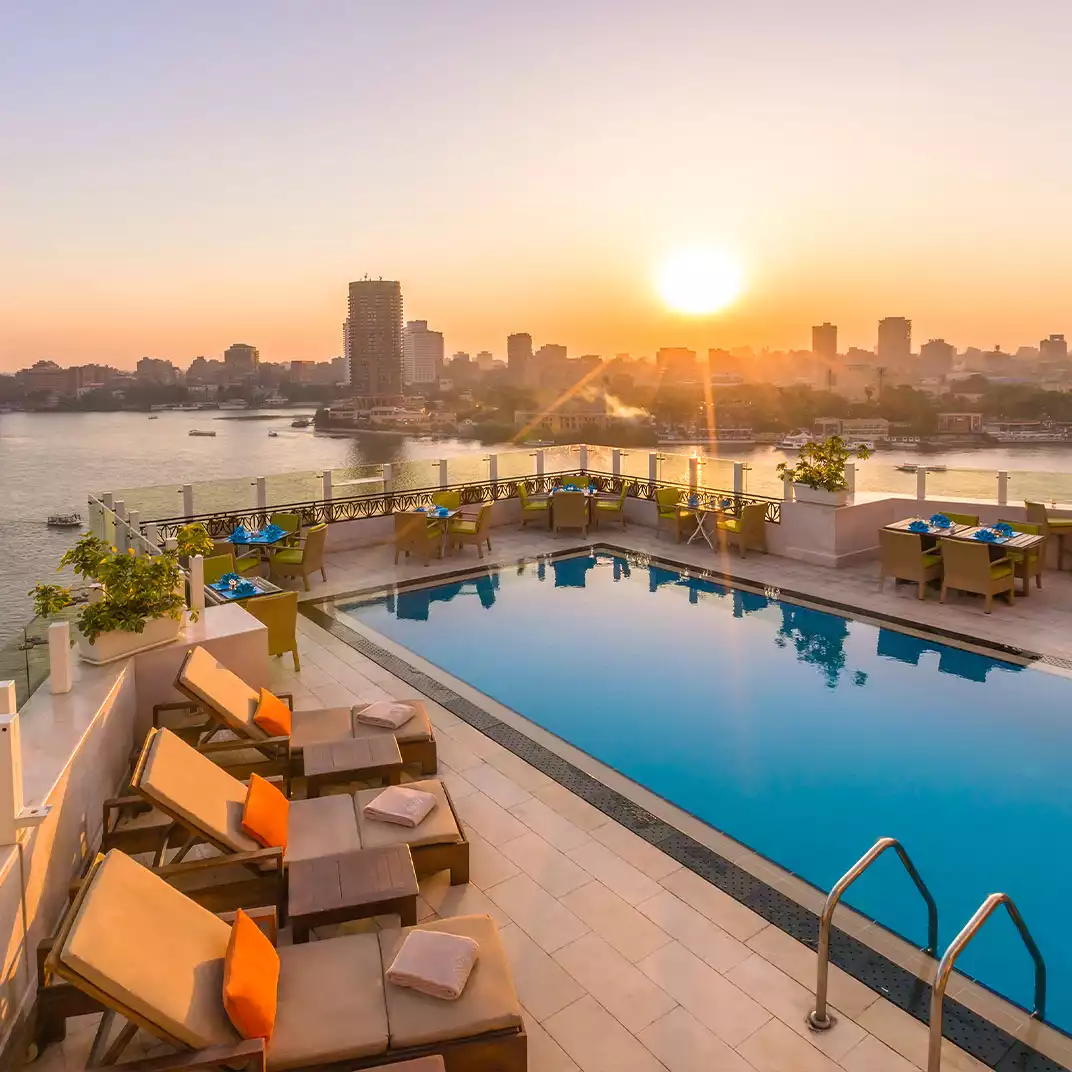 Kempinski Nile Hotel Garden City'nin şehir manzarası eşliğinde çekilmiş havuz görüntüsü ve şezlonglar.