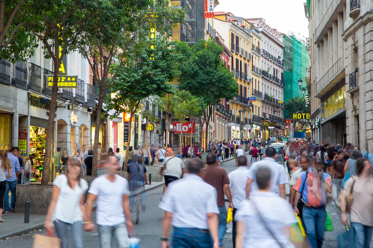 Madrid şehir merkezinde mağazaların bulunduğu geniş bir şehir caddesinde yürüyen kalabalık insan grubu
