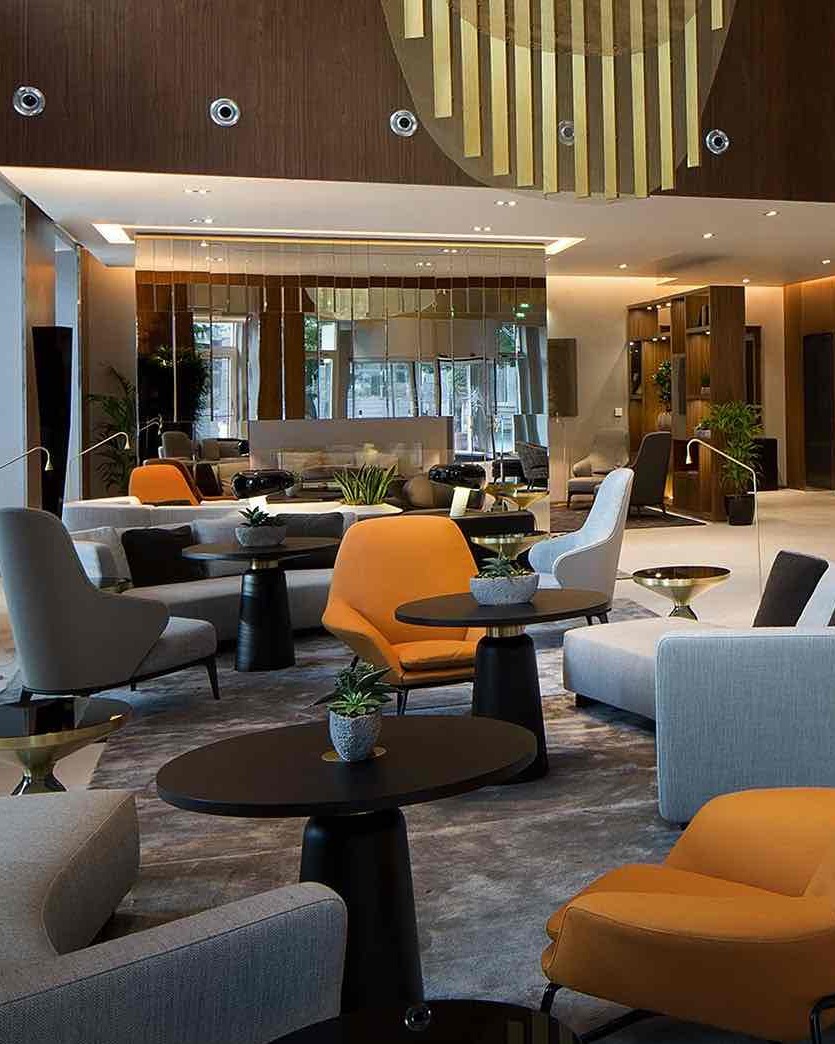 Skopje Marriott Hotel'in Makedonya Meydanı'ndaki geniş ve lüks lobisi, modern gri kanepeler, çarpıcı turuncu koltuklar, ahşap detaylı duvarlar ve şık aydınlatmalarla Üsküp seyahatinizde konforlu bir konaklama deneyimi vadediyor.
