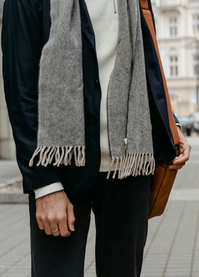 Gri atkı ve lacivert ceket kombinasyonu giyen bir kişinin şehir ortamında yürürken görüntülendiği minimalist sokak stili; modern, sade ve fonksiyonel moda detayları.