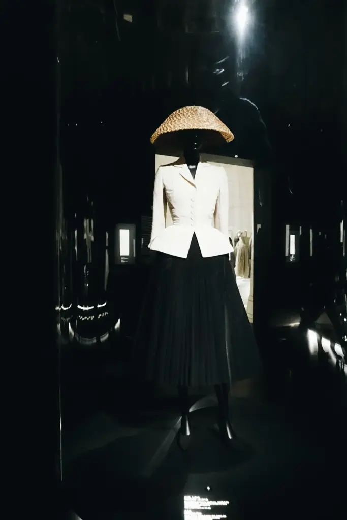 Dior’un ikonik Bar Suit tasarımını sergileyen, bej ceket ve pileli siyah etekten oluşan haute couture moda silueti.