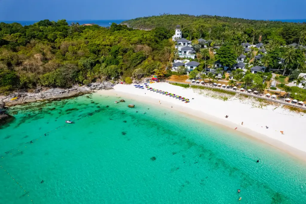Phuket'e yakın Racha Adaları'ndan birini kuşbakışı gösteren bu fotoğrafta, turkuaz suların berraklığında yüzen insanlar, bembeyaz kumlu sahilde sıralanmış rengarenk şemsiyeler ve ağaçlarla kaplı tepenin yamacında beyaz çatılı otel binaları dikkat çekiyor.