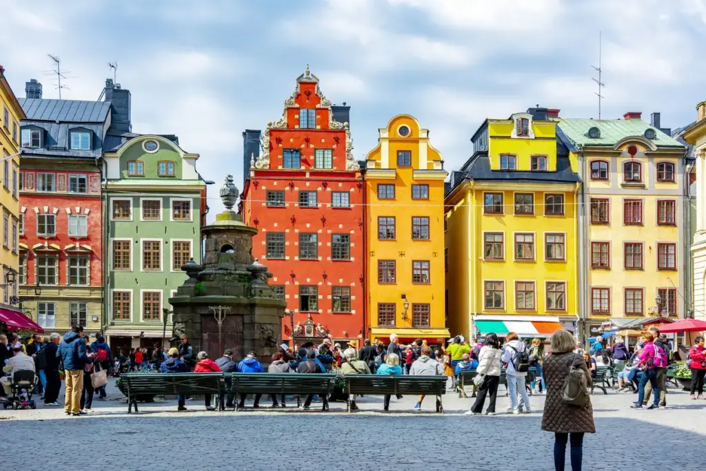 Stockholm'ün tarihi kalbi Gamla Stan'daki Stortorget Meydanı'nda, safran sarısı, kiremit kırmızısı ve nane yeşili gibi karakteristik binaların önünde toplanmış kalabalık, banklarda dinlenerek ve etrafta dolaşarak şehrin bu eşsiz gezilecek yerlerinden birinin canlı atmosferinin keyfini çıkarıyor.