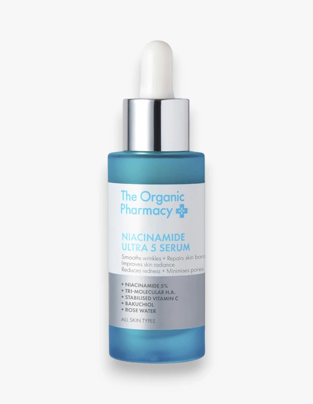 Beyaz bir arka plan üzerinde duran, The Organic Pharmacy Niacinamide Ultra 5 Serum adlı, beyaz damlalıklı ve parlak gümüş kapaklı, şeffaf turkuaz renkli cam şişe, kırışıklık ve gözenek karşıtı bakım serumu olarak konumlanıyor.
