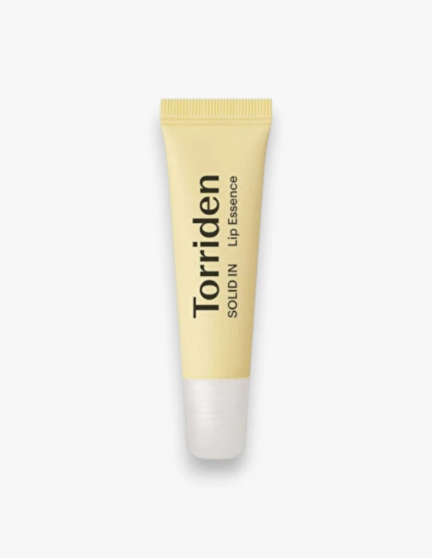 Açık krem renkli ve beyaz kapaklı Torriden Solid In Ceramide Lip Essence tüpü, üzerinde belirgin siyah harflerle Torriden, dikey olarak SOLID IN ve Lip Essence yazılarıyla, dudakları beslemeyi hedefleyen zengin içerikli bir dudak esansı ürününü sergiliyor.
