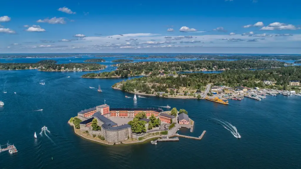 Stockholm Takımadaları'nda masmavi sularla çevrili küçük bir adacıkta, tarihi Vaxholm Kalesi'nin taş duvarları ve kırmızı çatılı binaları, yemyeşil adaların, hareketli bir limanın ve irili ufaklı teknelerin görüldüğü bu panoramik hava fotoğrafında, Kuzeyin En Rafine Rotası: Stockholm’de Gezilecek Yerler rehberimizde bahsettiğimiz önemli bir destinasyon olarak tüm ihtişamıyla yükseliyor.