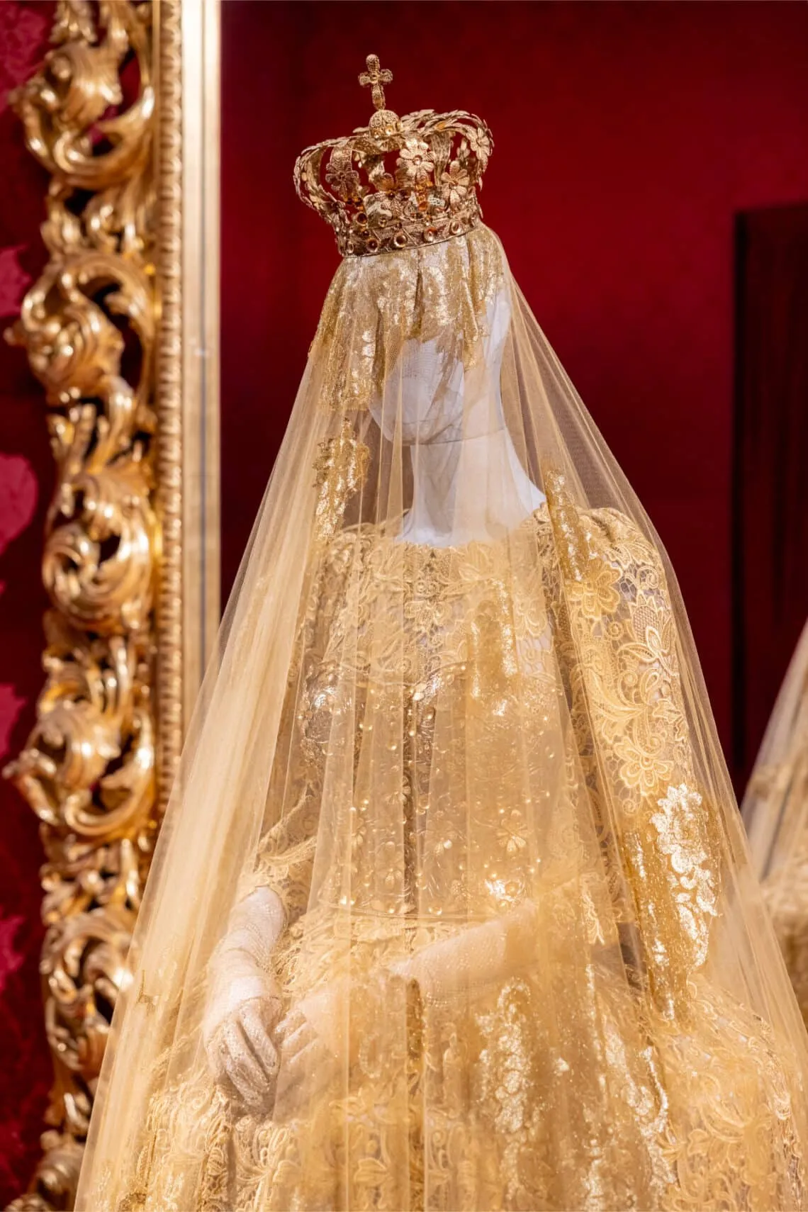 Altın taç ve ince tül detaylarla tamamlanan, dini ikonografiden ilham alan Dolce & Gabbana Alta Moda elbisesi; barok estetik ve kraliyet ihtişamını yansıtan sergi görünümü.
