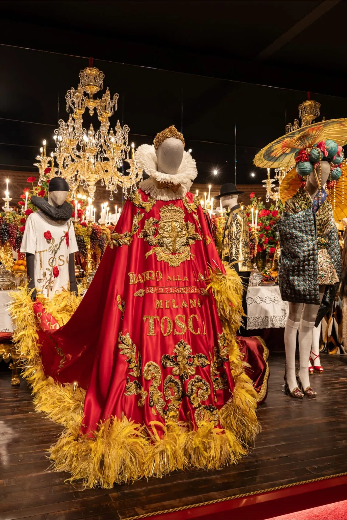 Kırmızı ve altın işlemeli dramatik pelerin tasarımıyla Dolce & Gabbana Alta Moda koleksiyonundan bir parça; teatral sunum, zanaatkârlık ve İtalyan mirası vurgusu.