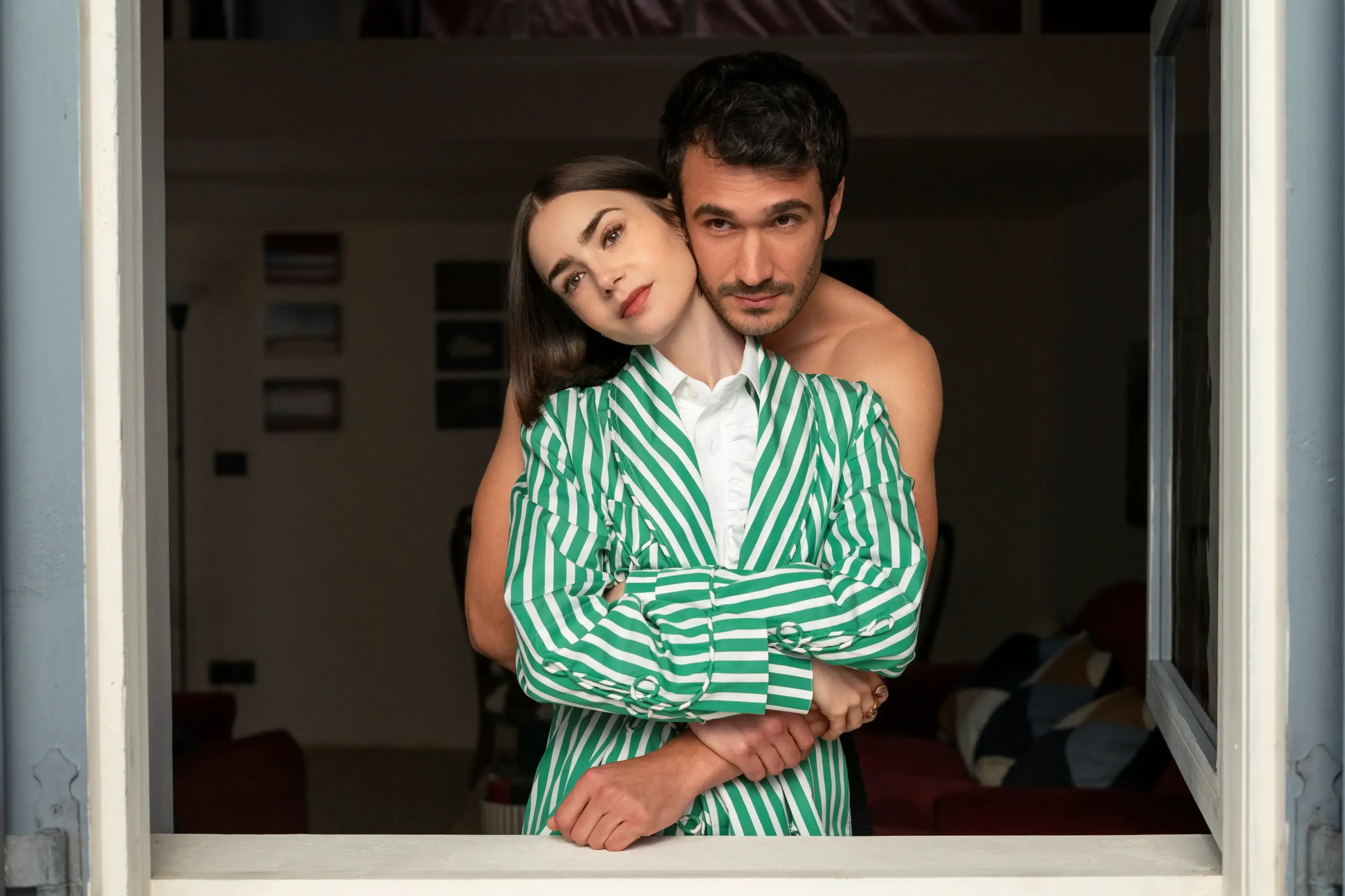 Emily in Paris dizisinde yeşil beyaz çizgili blazer takımla pencerede romantik ve samimi çift sahnesi.
