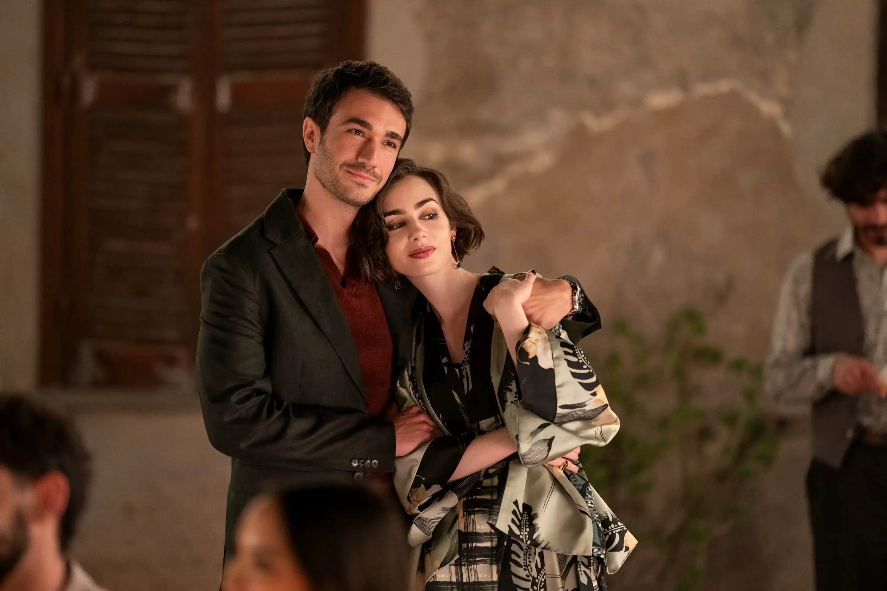 Emily in Paris dizisinde romantik bir akşam sahnesinde desenli elbise ve koyu ton takım elbise ile samimi çift anı.
