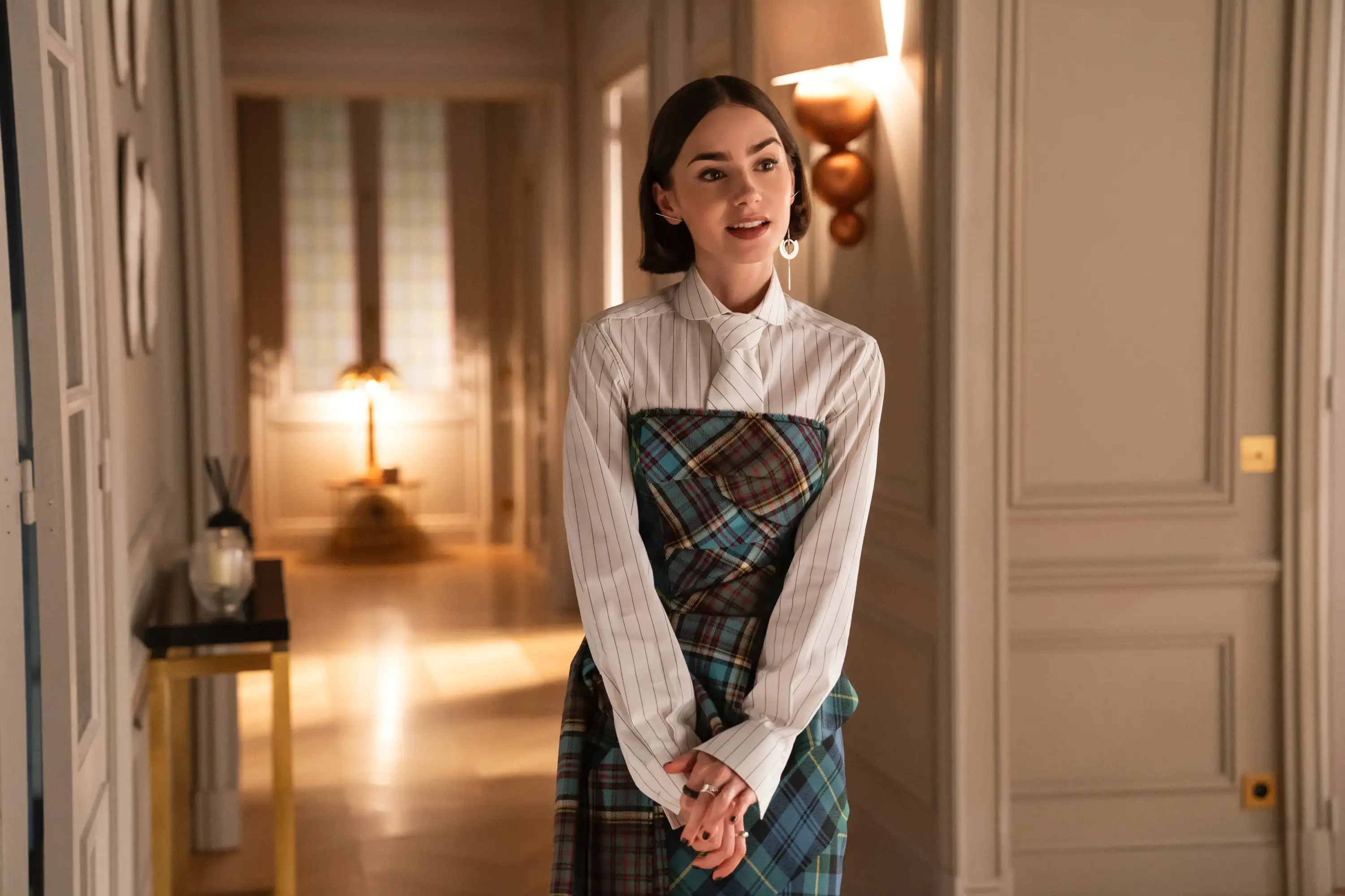 Emily in Paris dizisinde çizgili gömlek, korsaj kemer ve kalem etekle modern ofis şıklığını yansıtan yürüyüş sahnesi.
