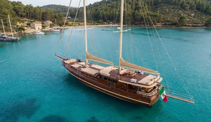 Çam ağaçlarıyla çevrili sakin bir koyda demirlemiş, ahşap gövdeli, İtalyan tipi bir gulet