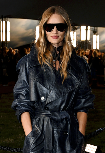 Uzun, dalgalı sarı saçları ve açık renk rujuyla şık bir görünüm sergileyen Rosie Huntington-Whiteley, siyah oversized siper tarzı güneş gözlüğü ve deri trençkotuyla oval yüz şekline uygun cesur bir stil örneği sunuyor.