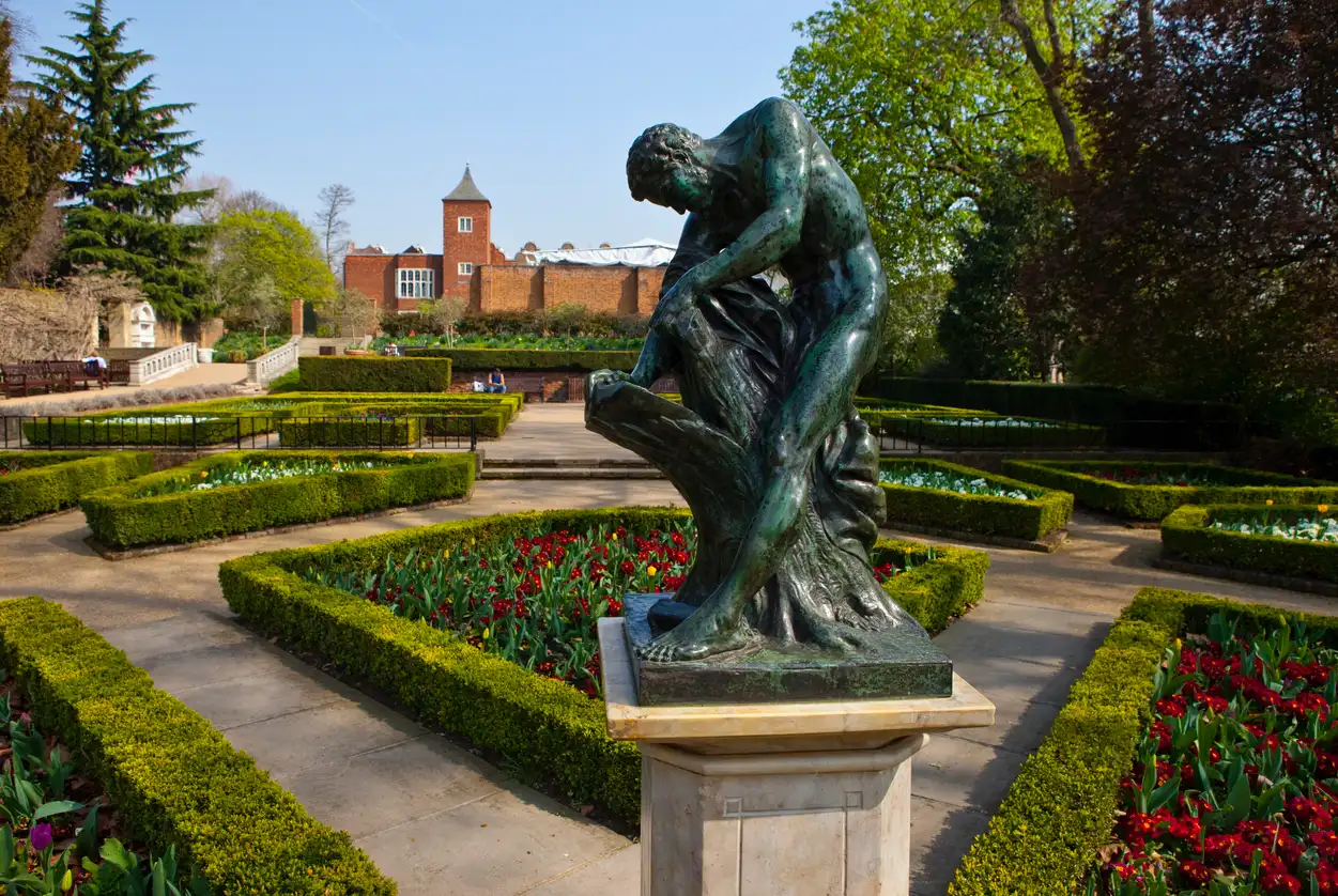 Londra’daki Holland Park’ta yer alan klasik bronz heykel; düzenli bahçeler, çiçek tarhları ve tarihi mimariyle çevrili sakin park manzarası.