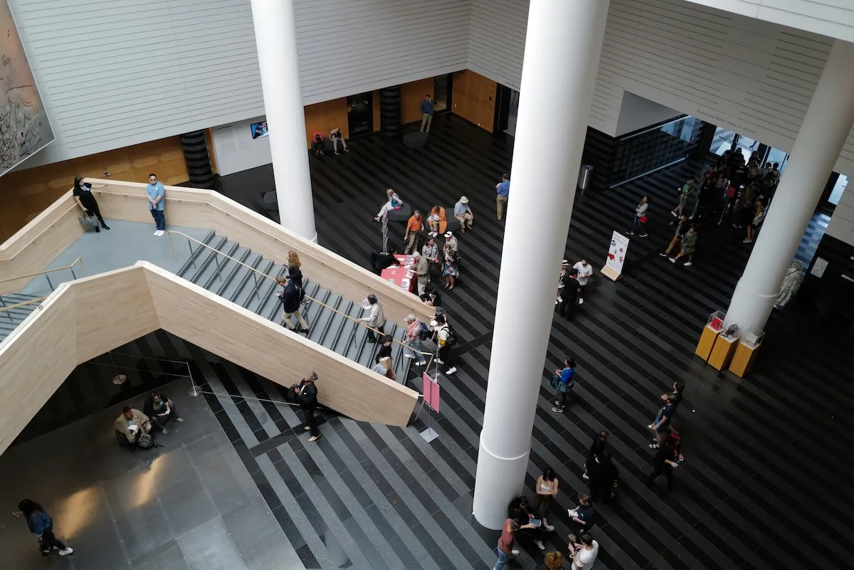 New York'taki Modern Sanat Müzesi'nin (MoMA) yüksek tavanlı, ferah ve modern iç mekanından kuşbakışı çekilen bu karede, binanın farklı katlarını birbirine bağlayan geniş ahşap merdivenlerde ve siyah beyaz desenli zeminde dolaşan, bir kısmı oturup dinlenen kalabalık ziyaretçiler, müzenin atmosferini deneyimliyor.