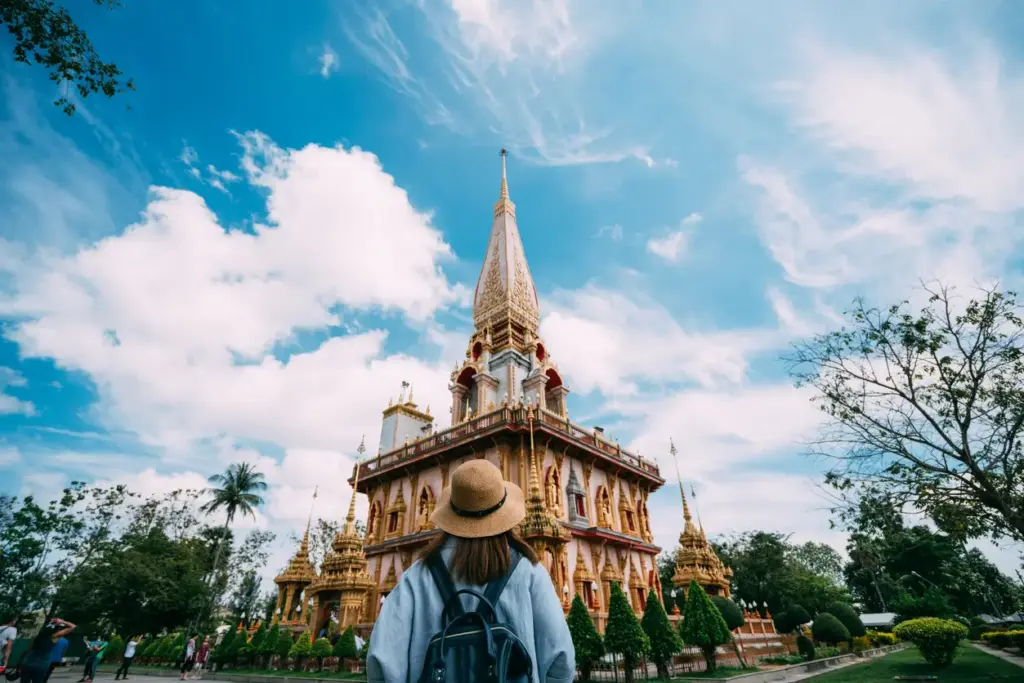 Phuket'in mistik ruhunu yansıtan, altın varaklı ve bembeyaz görkemli bir tapınağa, sırt çantalı ve şapkalı bir gezgin hayranlıkla bakarken, masmavi gökyüzü ve bulutlar bu eşsiz gezilecek yer manzarasını bütünlüyor.