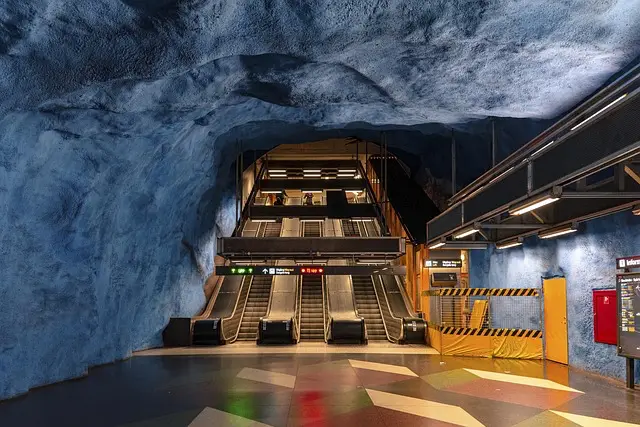 Stockholm Metrosu'nun eşsiz bir istasyonunda, mavinin tonlarıyla mağara benzeri boyanmış duvarlar ve tavan altında, yukarıya doğru çıkan kademeli yürüyen merdivenler, şehrin sanatsal yeraltı dünyasının ziyaretçiler için önemli bir gezilecek yer olduğunu gösteriyor.