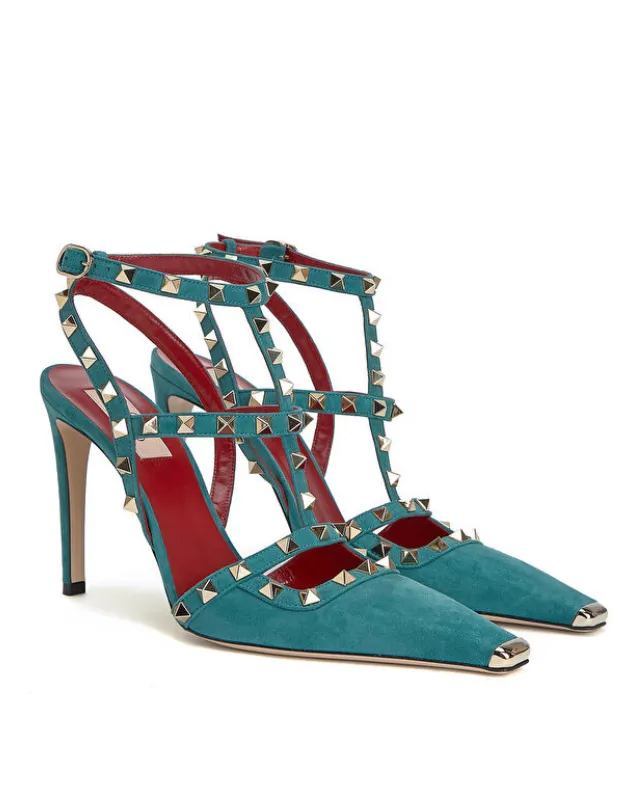 Parlak altın piramit zımbalarla süslenmiş, turkuaz süet deri Valentino Garavani Rockstud topuklu sandaletler, sivri burunları ve metal burun uçlarıyla dikkat çekerek tüm zamanların en ikonik ayakkabı tasarımlarından biri olarak öne çıkıyor.