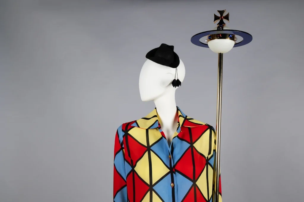 Canlı kırmızı, sarı ve mavi geometrik desenleriyle dikkat çeken Vivienne Westwood tasarımı; punk ruhu ve grafik moda diliyle öne çıkan ikonik sergi görünümü.