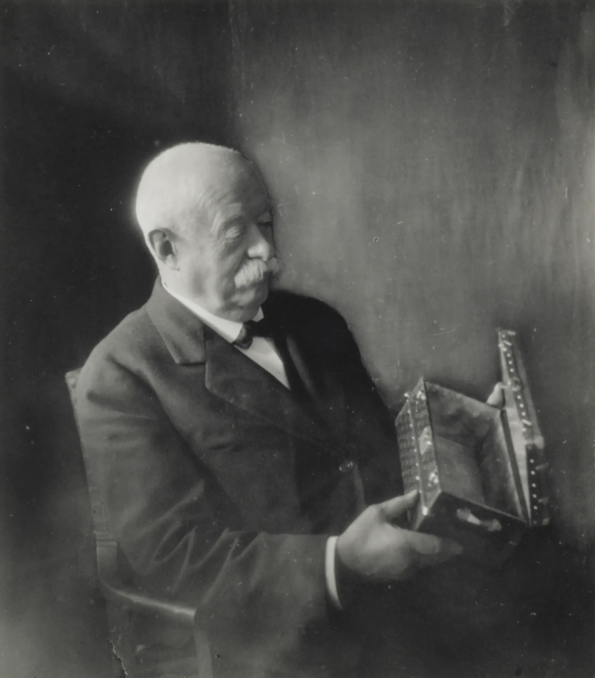 1930'lu yıllara ait bu eski siyah beyaz portrede, Louis Vuitton Monogram'ının yaratıcısı Georges Vuitton, zarif bıyıklı yaşlı bir beyefendi olarak elindeki işlemeli küçük kutuya derin bir ilgiyle bakarak markanın zengin 130 yıllık hikâyesini yansıtan bir sahne sunuyor.