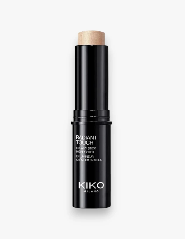 Kiko Milano'nun Radiant Touch Creamy Stick Highlighter ürünü, beyaz sade bir arka plan üzerinde dikey olarak konumlandırılmış, parlak siyah silindirik ambalajından dışarı çıkan ışıltılı ve açık bej renkteki kremsi aydınlatıcı formuyla dikkat çekiyor.