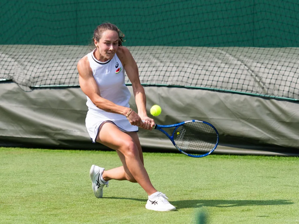 Zeynep Sönmez, Wimbledon 2024 elemelerinde çim kortta iki elle backhand vuruşu yaparken.