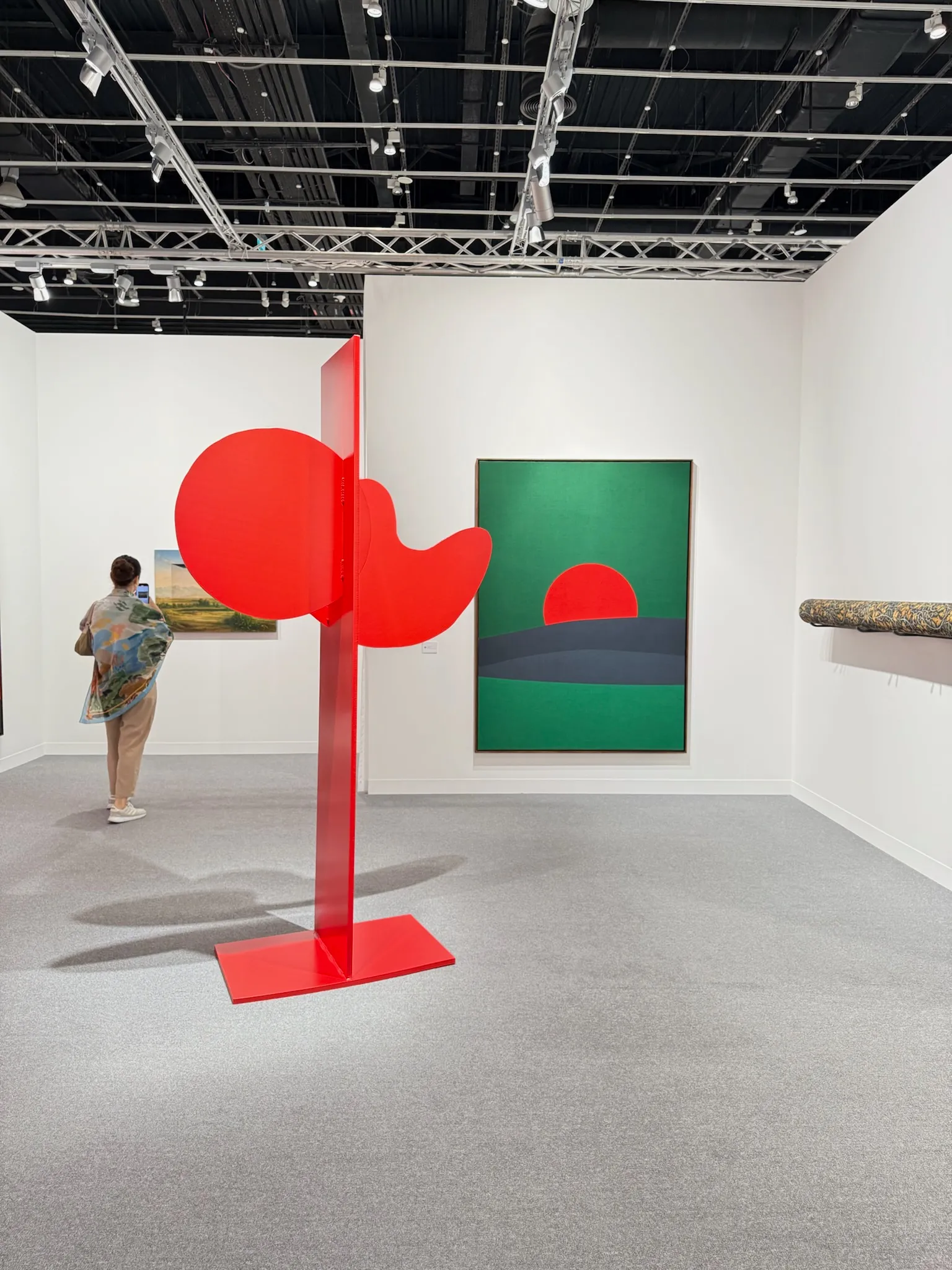 Abu Dhabi Art’ta kırmızı heykel yerleştirmesi ve arka planda geometrik kompozisyonlu çağdaş resimlerin yer aldığı sergi alanı
