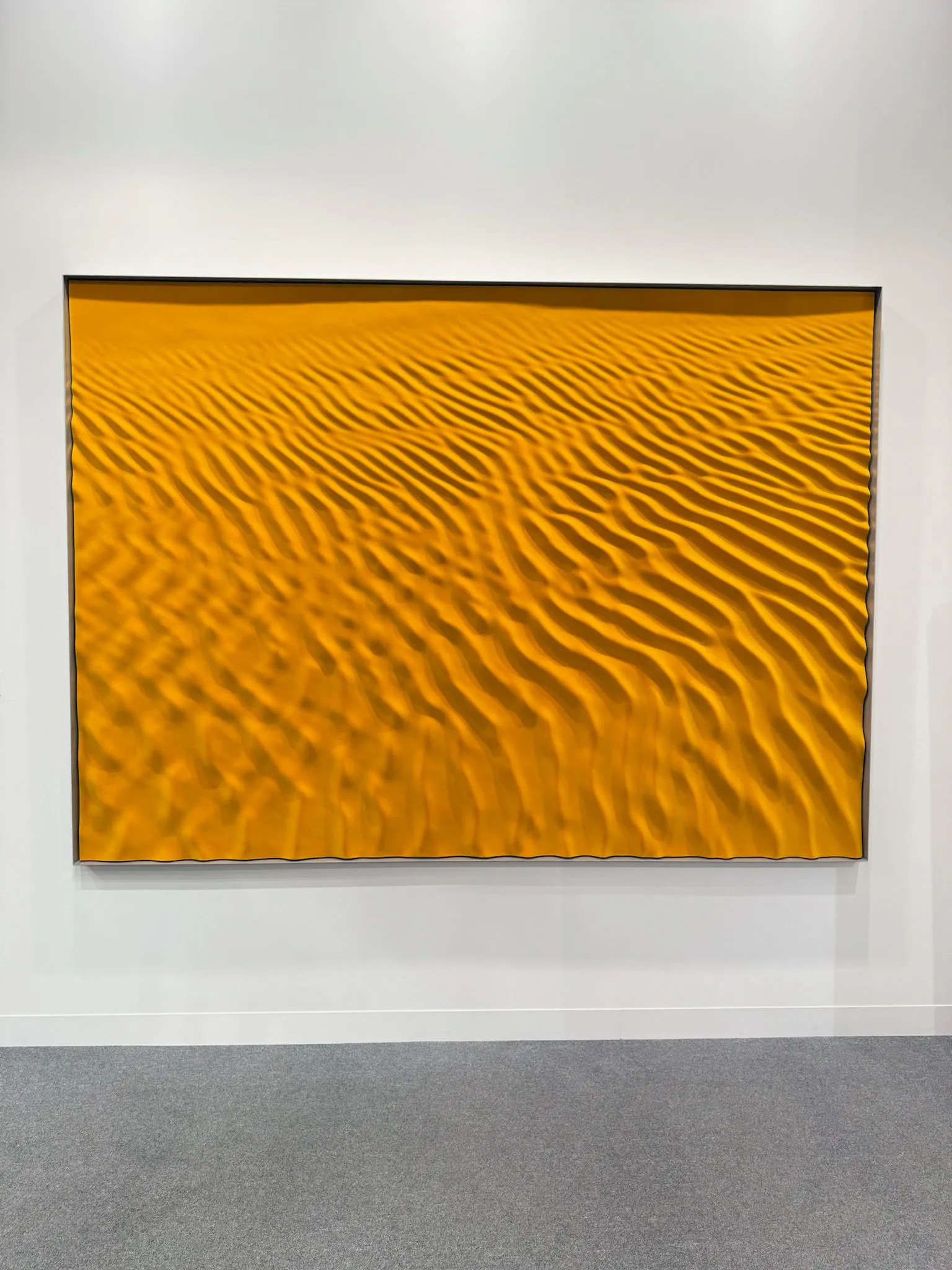 Abu Dhabi Art’ta sarı tonların hâkim olduğu, dalga dokulu soyut bir resmin sergilendiği galeri duvarı