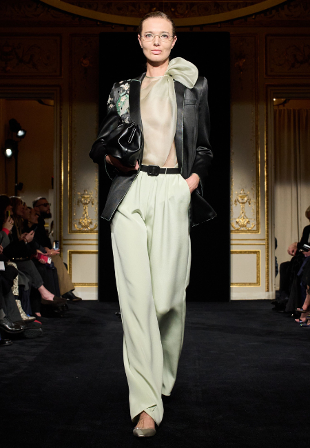 Armani Privé 2026 İlkbahar–Yaz haute couture defilesinde podyumda sunulan, siyah deri ceket, transparan ipek üst ve pastel yeşil yüksek bel pantolondan oluşan modern couture kombin.