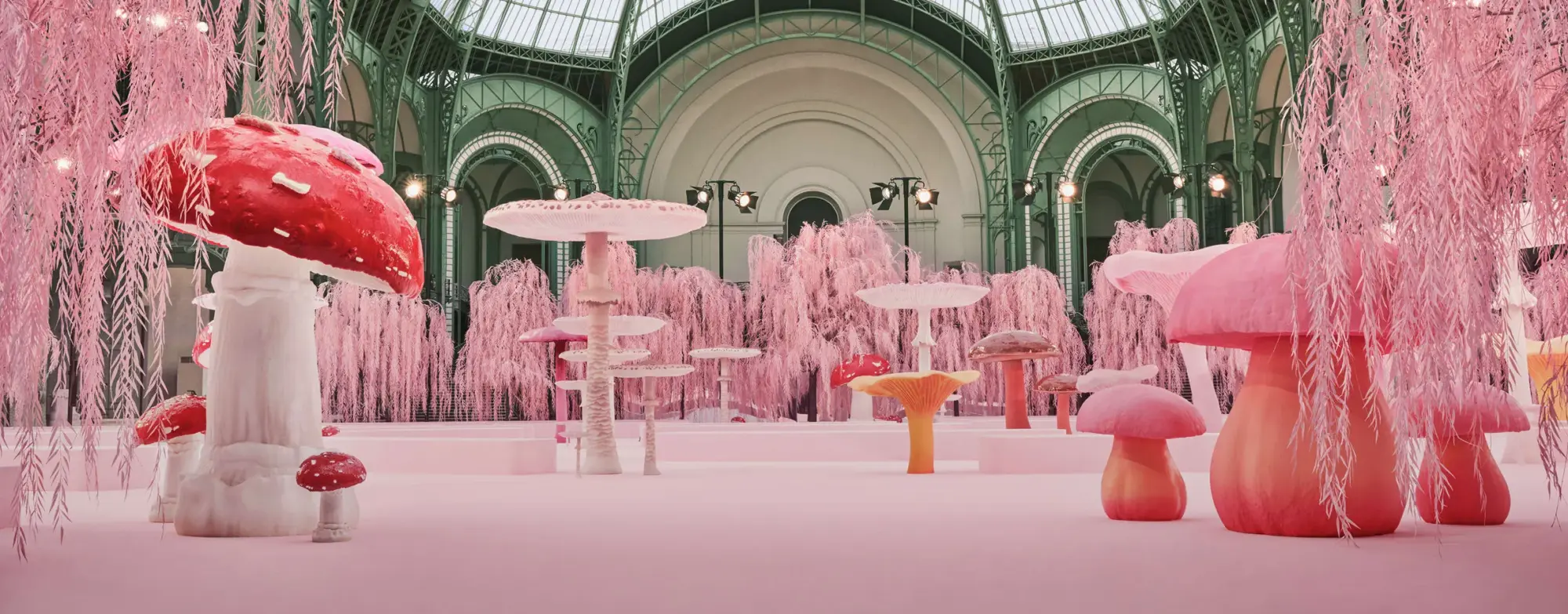 Chanel 2026 İlkbahar-Yaz Haute Couture defile mekânı: Pembe tonlarda mantar heykelleri, fantezi bahçe dekoru ve Grand Palais mimarisiyle kurgulanan masalsı podyum sahnesi.