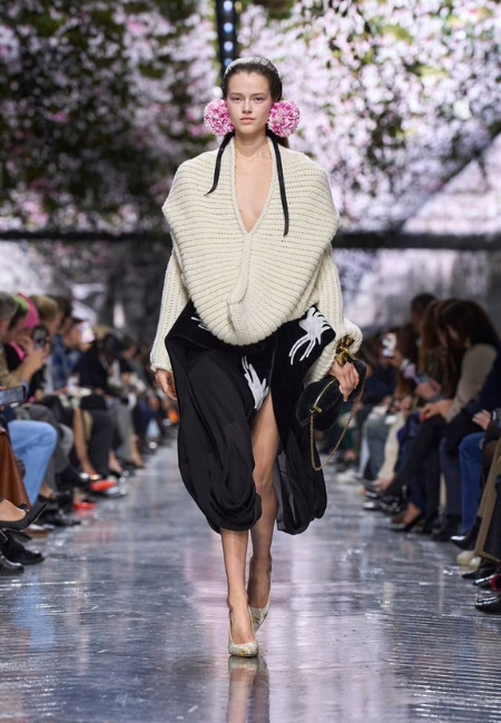 Dior 2026 couture koleksiyonunda krem örgü üst ve siyah drapeli etekle modern romantizmi yansıtan podyum stili.