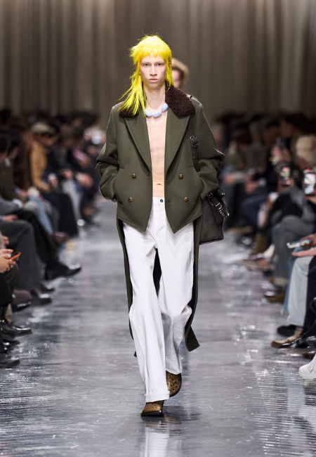 Dior 2026 sonbahar kış erkek defilesi, kürk yakalı haki ceket ve beyaz pantolon ile podyum görünümü.