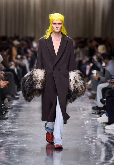 Dior 2026 sonbahar kış erkek giyim defilesi, kürk manşetli uzun siyah palto ve denim pantolon stili.