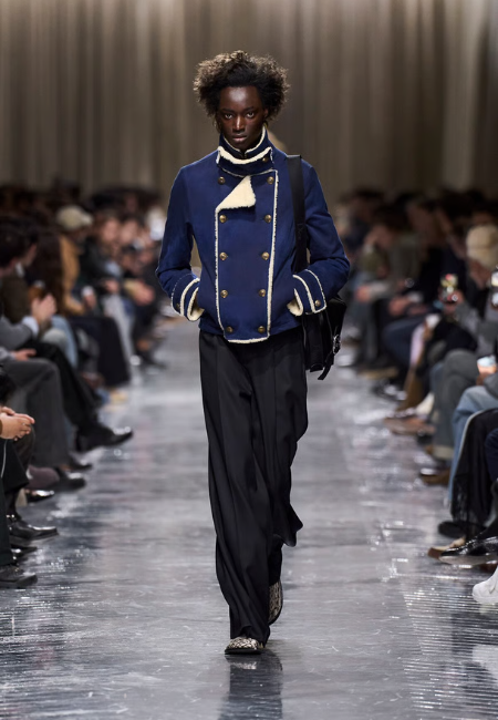 Dior 2026 sonbahar kış erkek koleksiyonu, lacivert askeri ceket ve geniş pantolon ile podyum görünümü.
