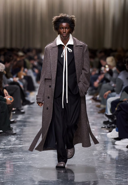 Dior 2026 sonbahar kış erkek koleksiyonu, uzun palto ve fiyonklu gömlek ile modern podyum görünümü.