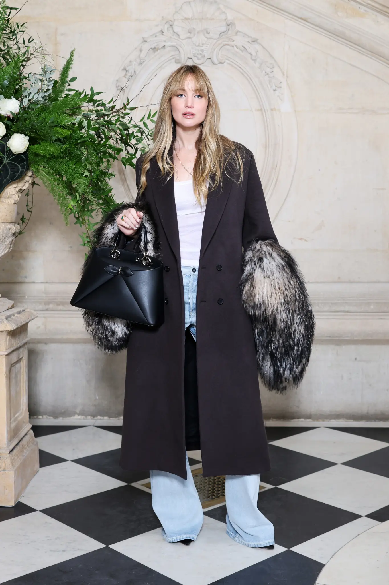 Jennifer Lawrence Dior 2026 Couture defilesinde kahverengi palto ve kürk manşetli casual şıklık.