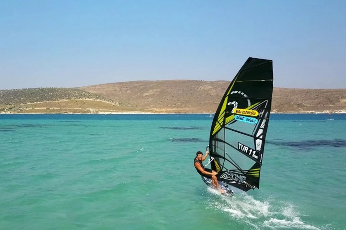 Alaçatı, Türkiye’de sörf yapılacak yerler arasında windsurf altyapısıyla öne çıkarken berrak sularda yelkeniyle ilerleyen bir sporcu.