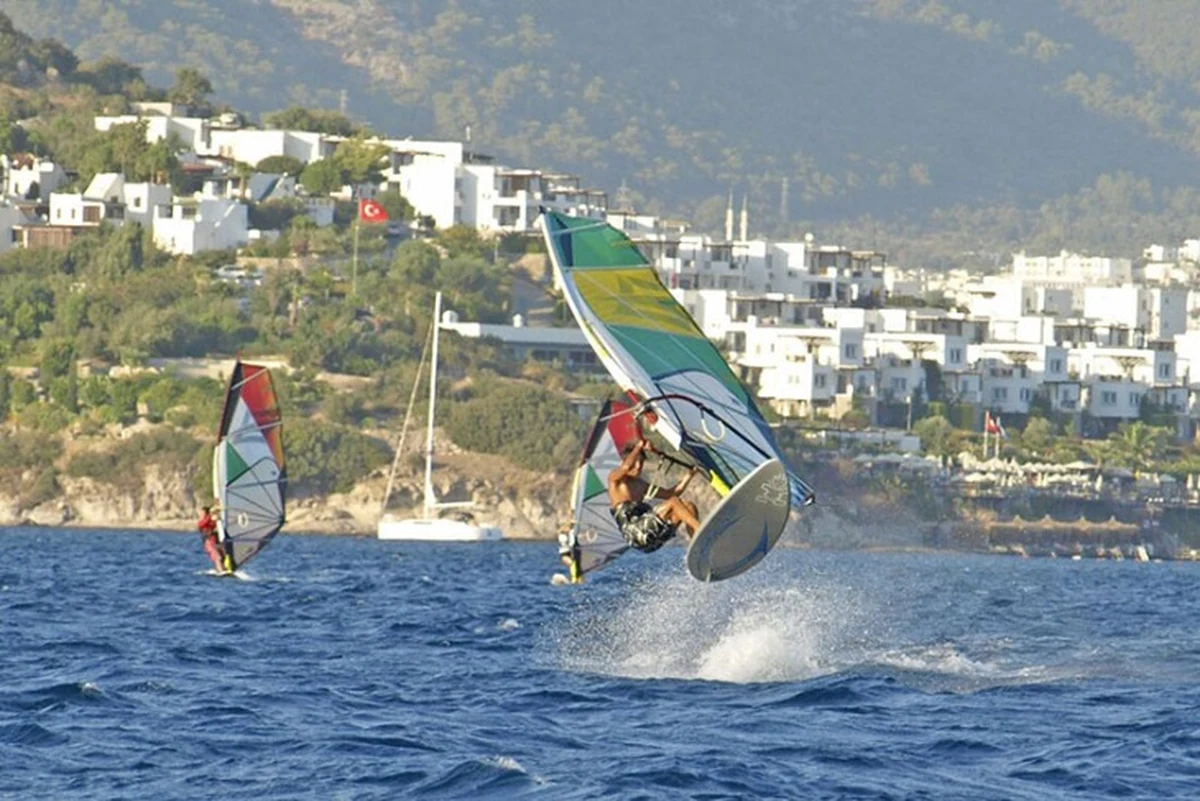 Bitez, Türkiye’de sörf yapılacak yerler arasında erişilebilir rotalardan biri olarak masmavi koyda windsurf yapan bir sporcuyla görülüyor.