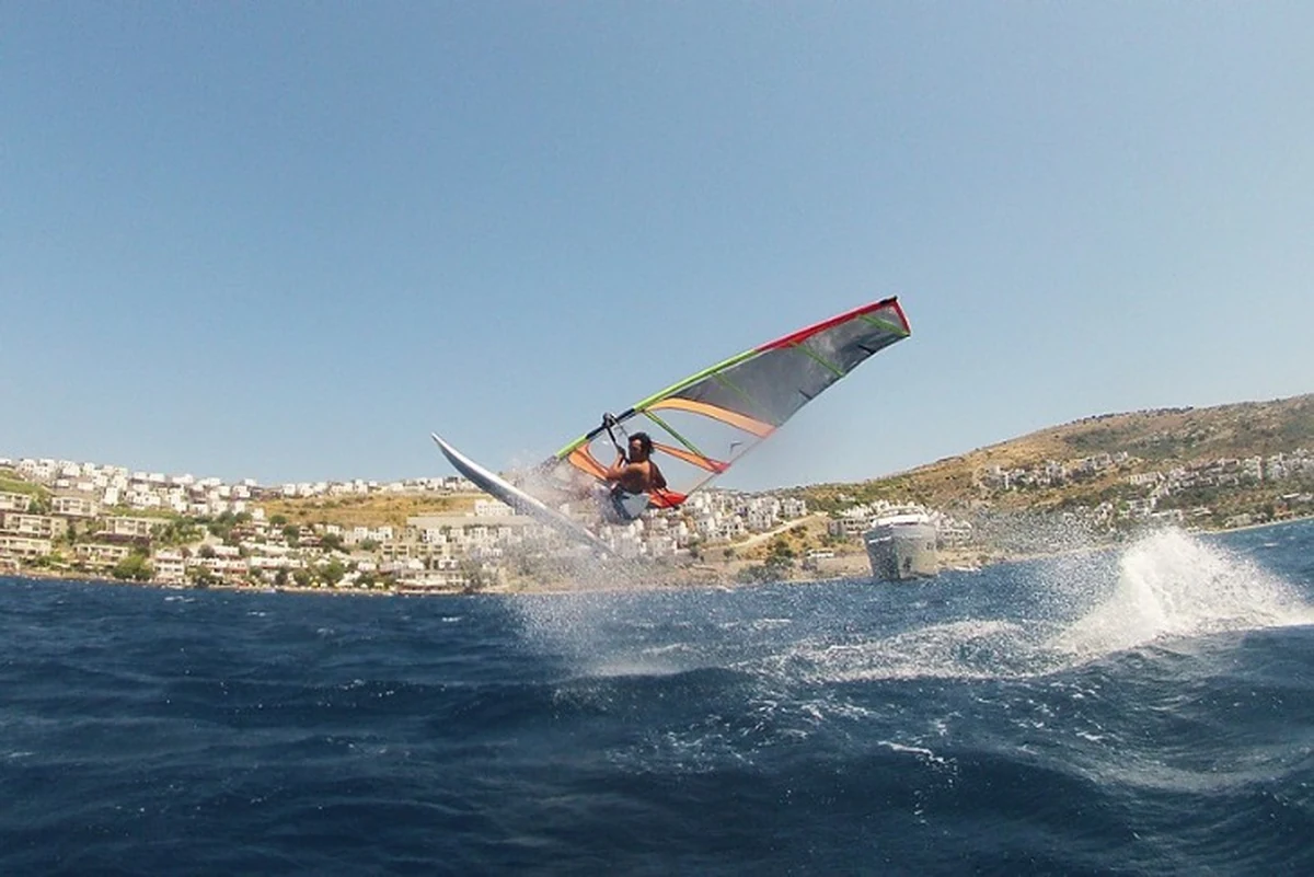 Gündoğan, Türkiye’de sörf yapılacak yerler arasında dengeli koy koşullarıyla öne çıkarken denizin üzerinde sıçrayan bir windsurfçü.