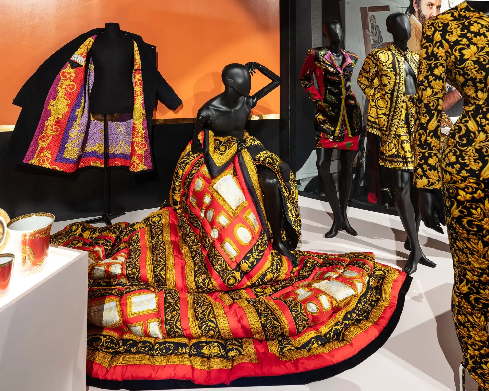 Gianni Versace moda sergisinden çekilen bu fotoğrafta, altın varaklı ve barok desenlerle zenginleştirilmiş siyah, kırmızı ve mor tonlarında lüks tasarımlar taşıyan cansız mankenler görülüyor; ön planda oturur pozisyonda olanın üzerindeki hacimli, kapitone giysi ve arka plandaki açık siyah ceketin iç astarındaki canlı motifler, dünyadaki moda sergilerinin özgün ve çarpıcı estetiğini gözler önüne seriyor.