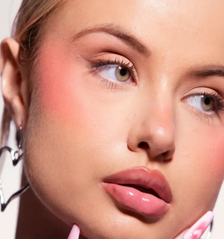 Huda Beauty modeli yanaklarında turuncu likit allık görünümü ile poz veriyor