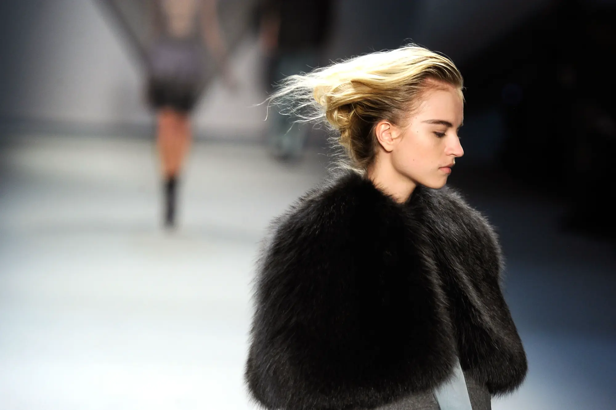 Podyumda siyah kürk görünümlü dış giyimle yürüyen model; moda dünyasında hayvan dostu alternatifler ve etik lüks tartışması.