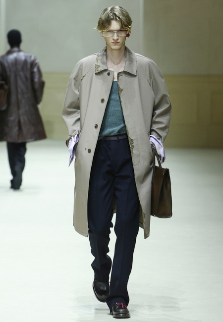 Prada 2026 sonbahar kış erkek koleksiyonu bej trench coat, mavi triko ve lacivert pantolon ile minimal runway kombini.
