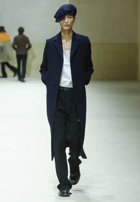 Prada 2026 sonbahar kış erkek koleksiyonu lacivert uzun palto, beyaz atlet, siyah pantolon ve bere ile minimal runway stili.