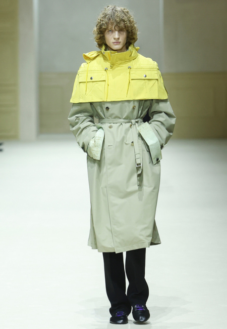 Prada 2026 erkek moda haftası sarı kapüşonlu parka detaylı gri trench coat, kuşaklı silüet ve spor ayakkabı ile modern dış giyim kombini.