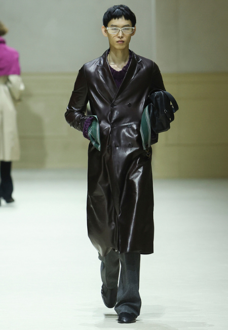 Prada 2026 erkek giyim defilesi kahverengi deri uzun palto, bordo katmanlı üst ve gri pantolon ile sofistike stil.