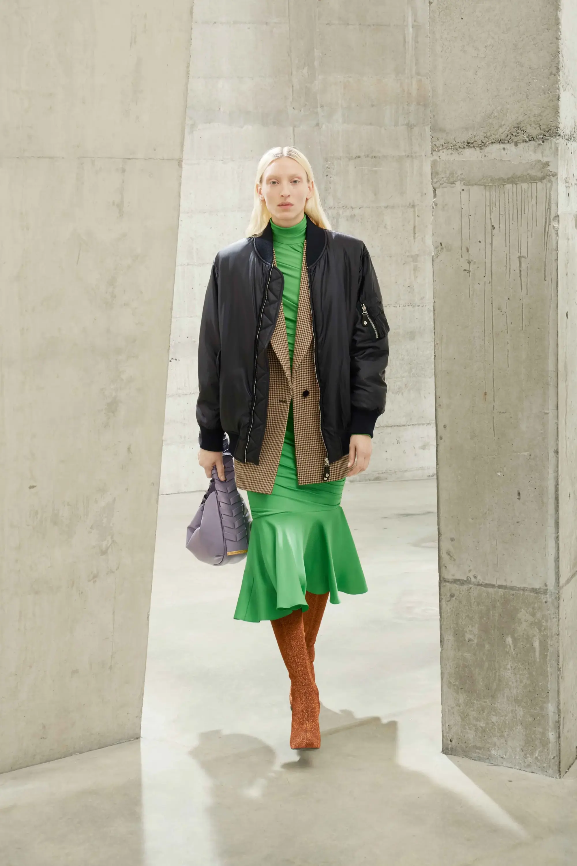 Stella McCartney Sonbahar/Kış 2021 koleksiyonundan yeşil elbise, siyah bomber ceket ve diz üstü kahverengi çizmelerle modern sürdürülebilir moda silüeti.