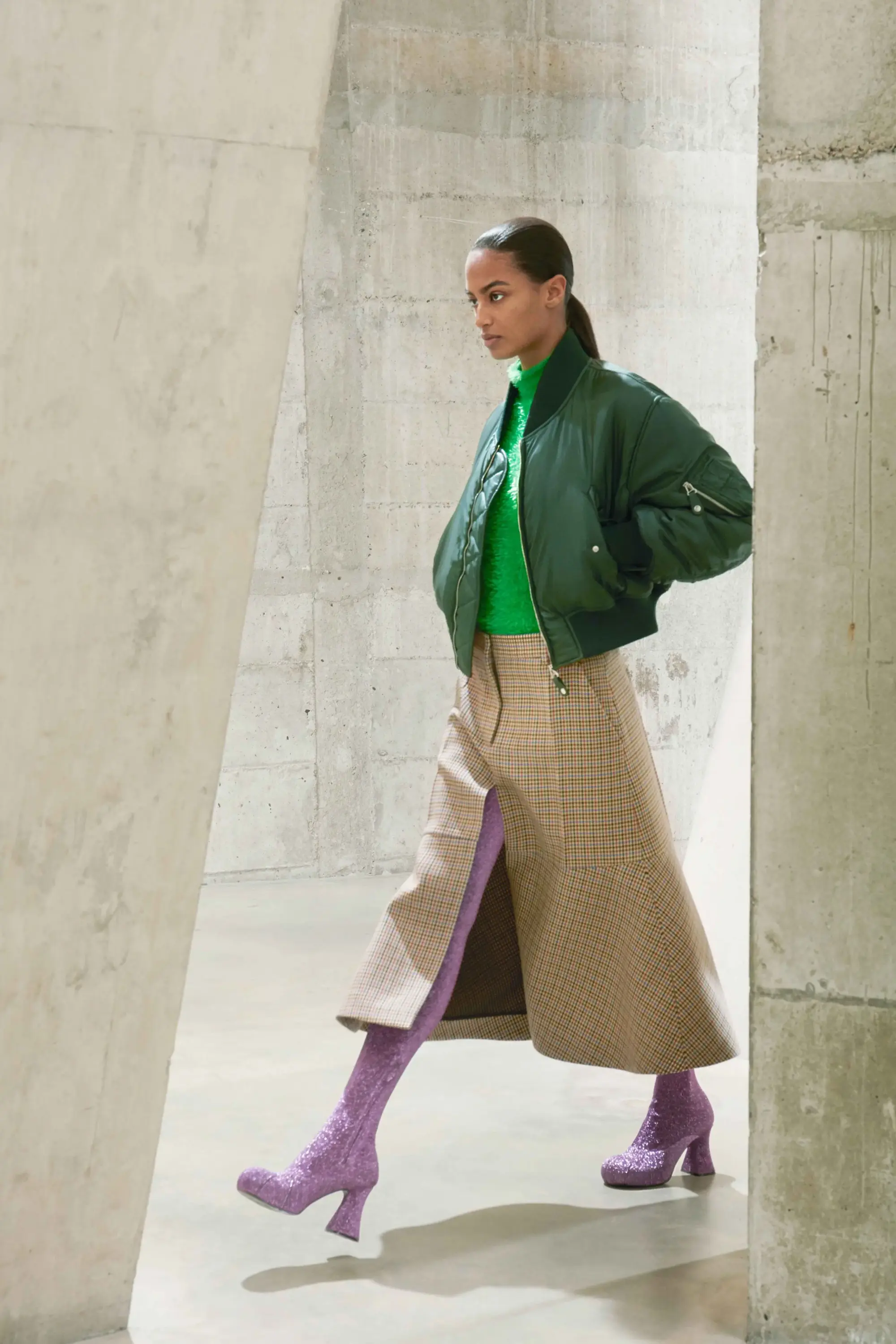 Stella McCartney Sonbahar/Kış 2021 defilesinden yeşil bomber ceket, desenli midi etek ve mor topuklu botlarla güçlü renk kontrastları.
