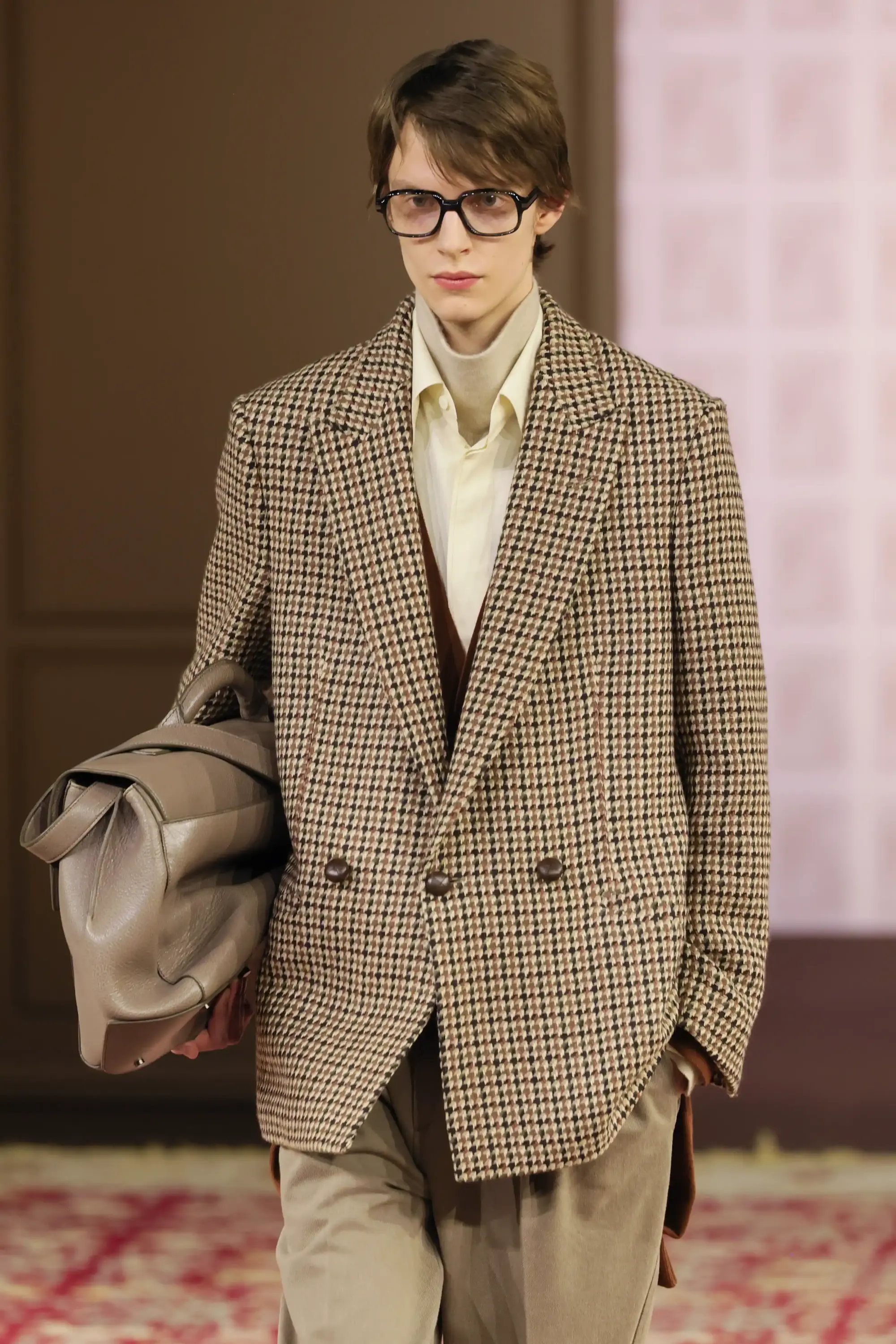 Zegna 2026 Sonbahar/Kış defilesinde kahverengi kazayağı desenli çift düğmeli blazer, bej boğazlı triko ve oversize gri deri çanta ile modern klasik erkek giyim görünümü.